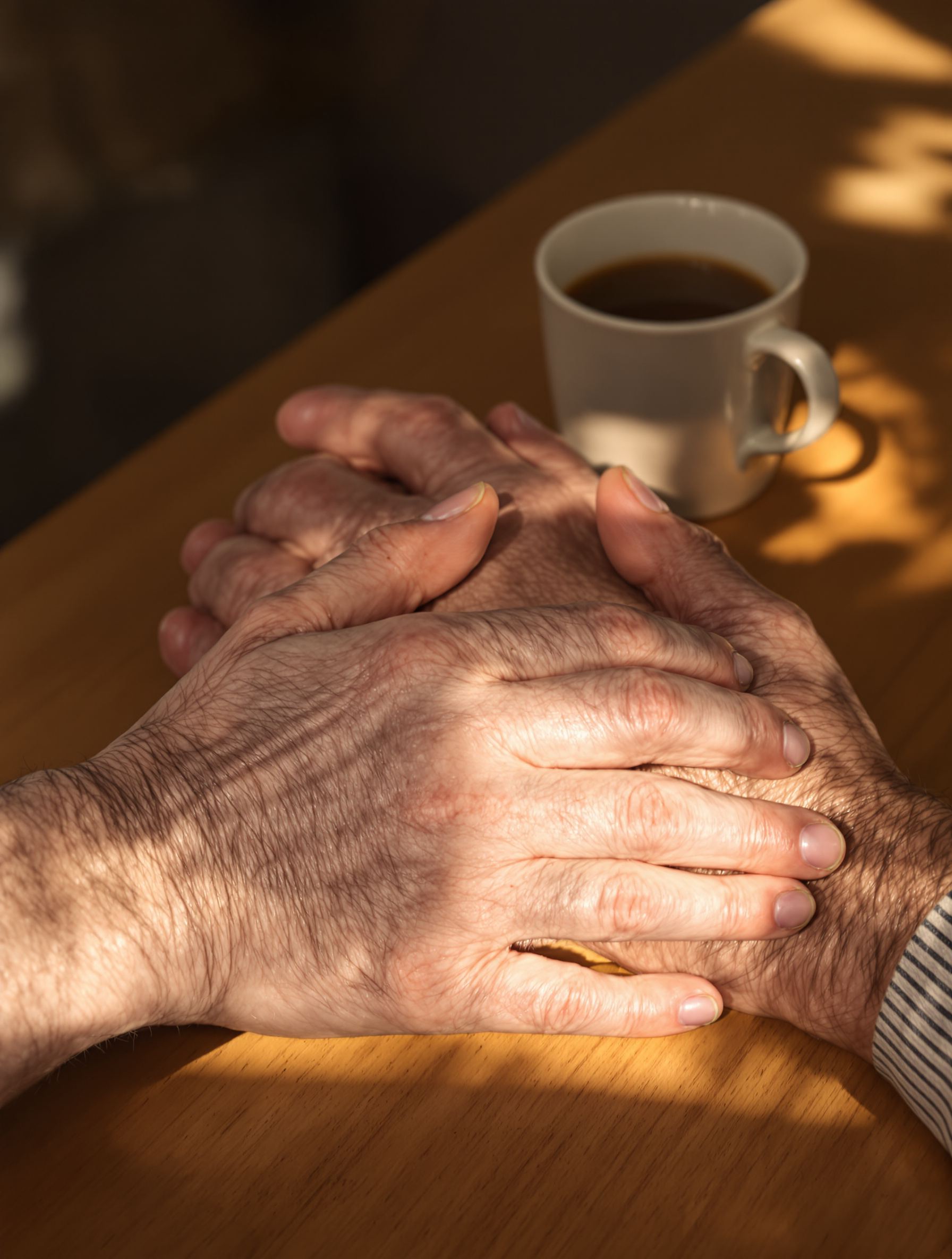 Deux paires de mains, l'une plus jeune et l'autre plus âgée, posées sur une table à côté d'une tasse de café. L'image évoque le soutien, la transmission et le répit.